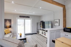 A modern living room with a sofa, coffee table, and a TV. There's a sliding glass door leading to a balcony. - Bougie Barn 5 mi to Silverwood Theme Park! (Athol)