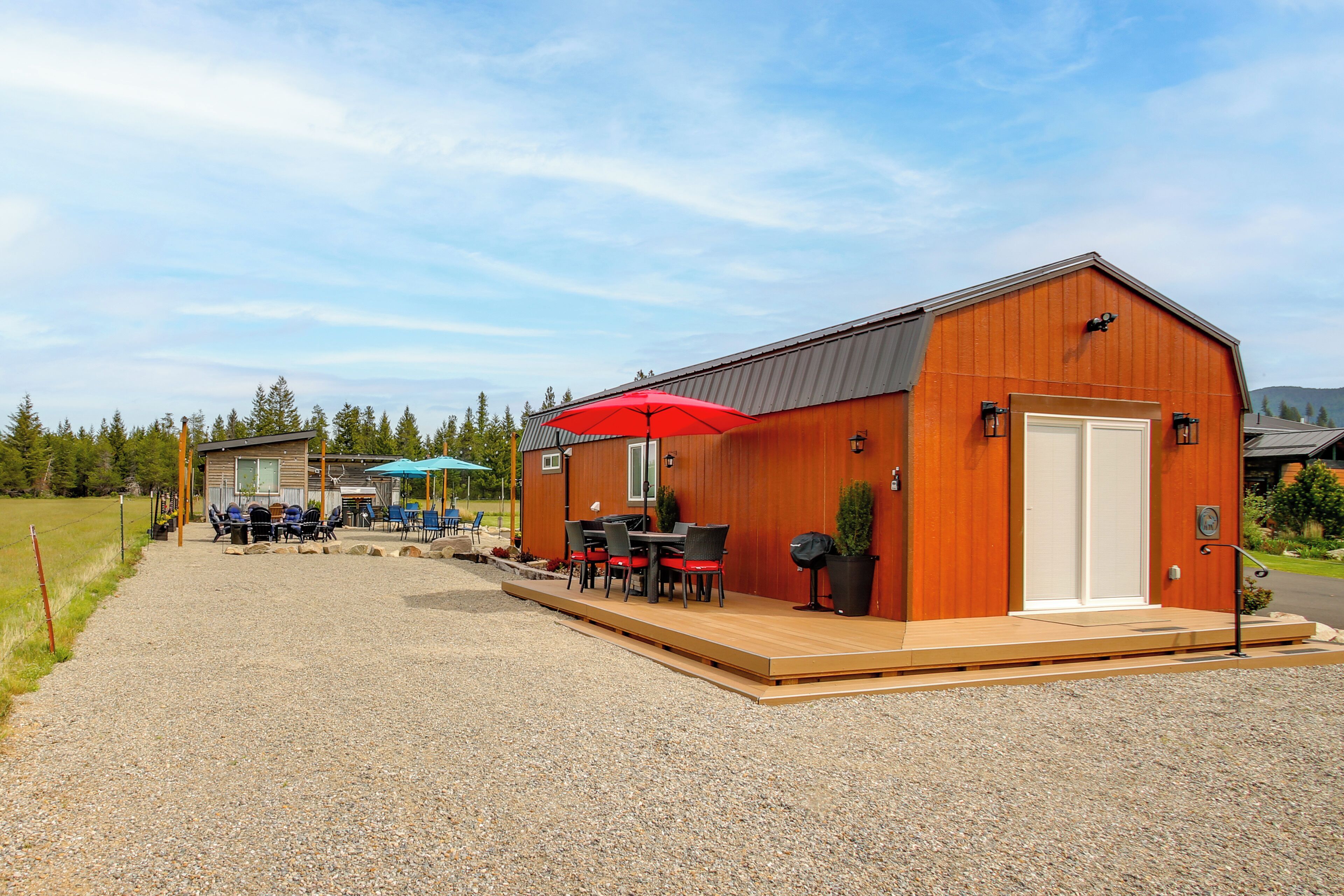 Un bâtiment à l’extérieur en bois, doté d’un patio couvert avec des tables et des chaises, et d’une allée gravillonnée.