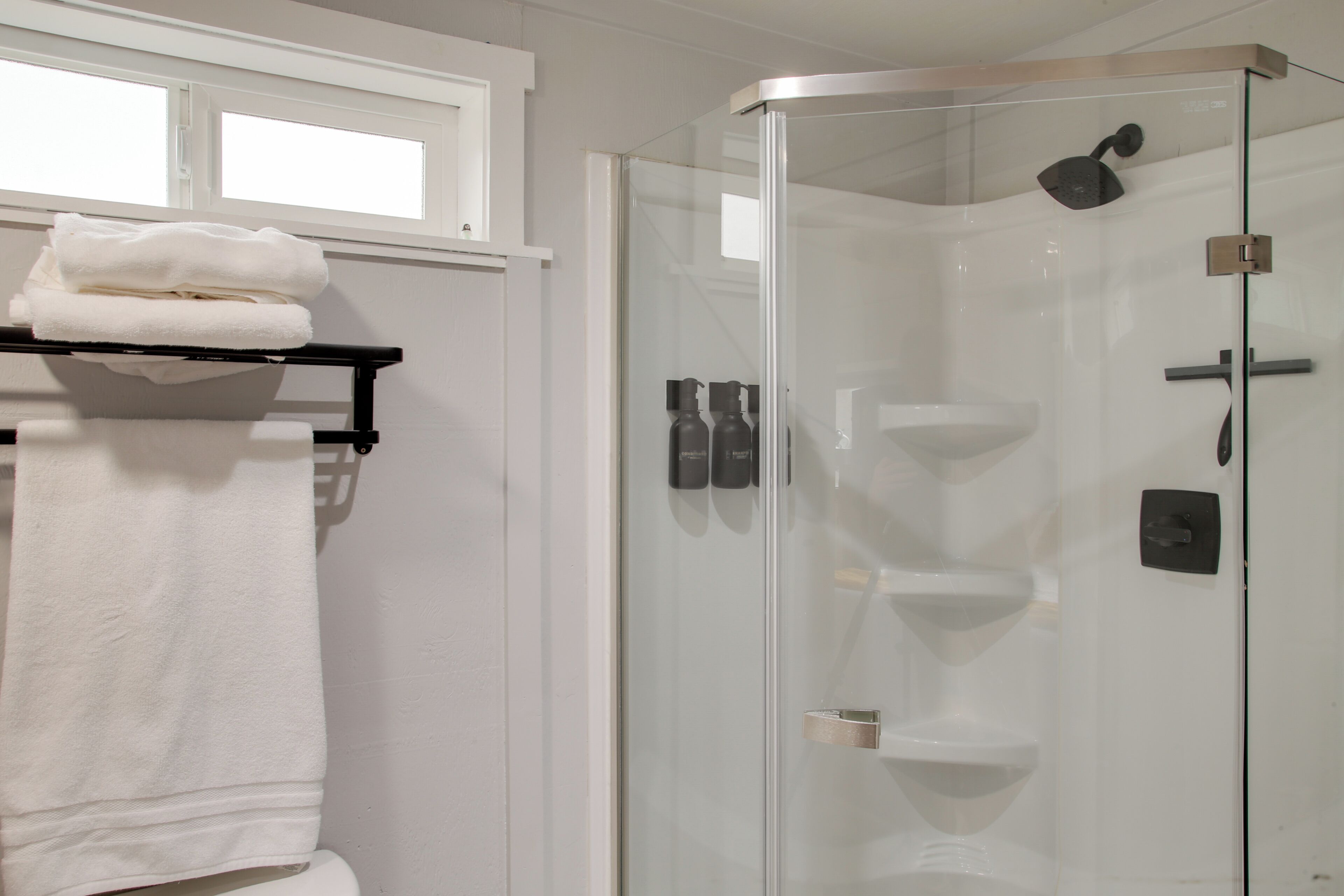 A modern bathroom with a glass-enclosed shower, a white sink, and a towel rack with folded towels.