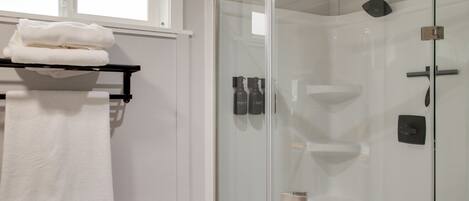 A modern bathroom with a glass-enclosed shower, a white sink, and a towel rack with folded towels.