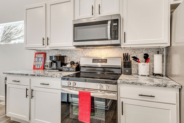 A modern kitchen with white cabinets, a stainless steel microwave, a black stovetop oven, and a red towel hanging.