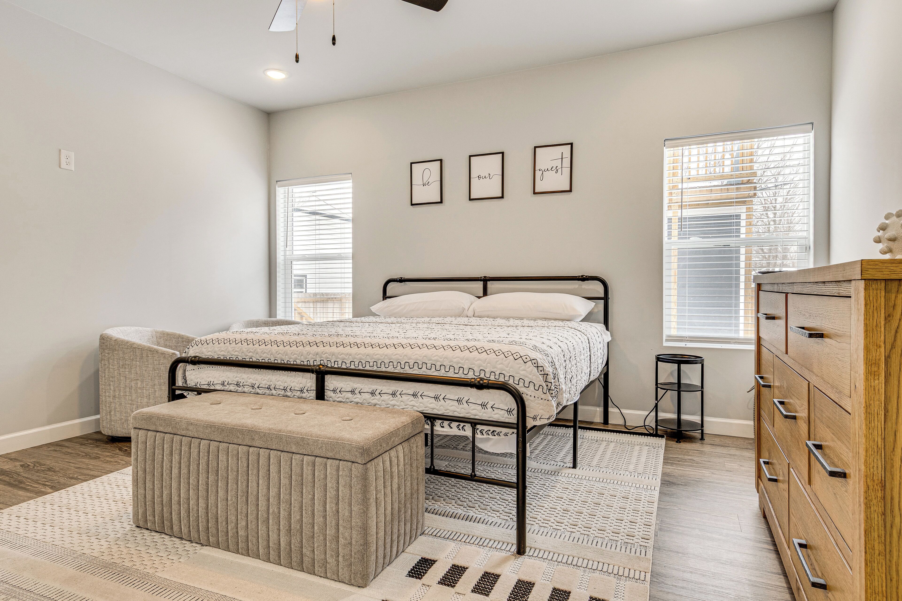 Une chambre à coucher avec un lit, une commode en bois, un banc et une fenêtre avec des stores.
