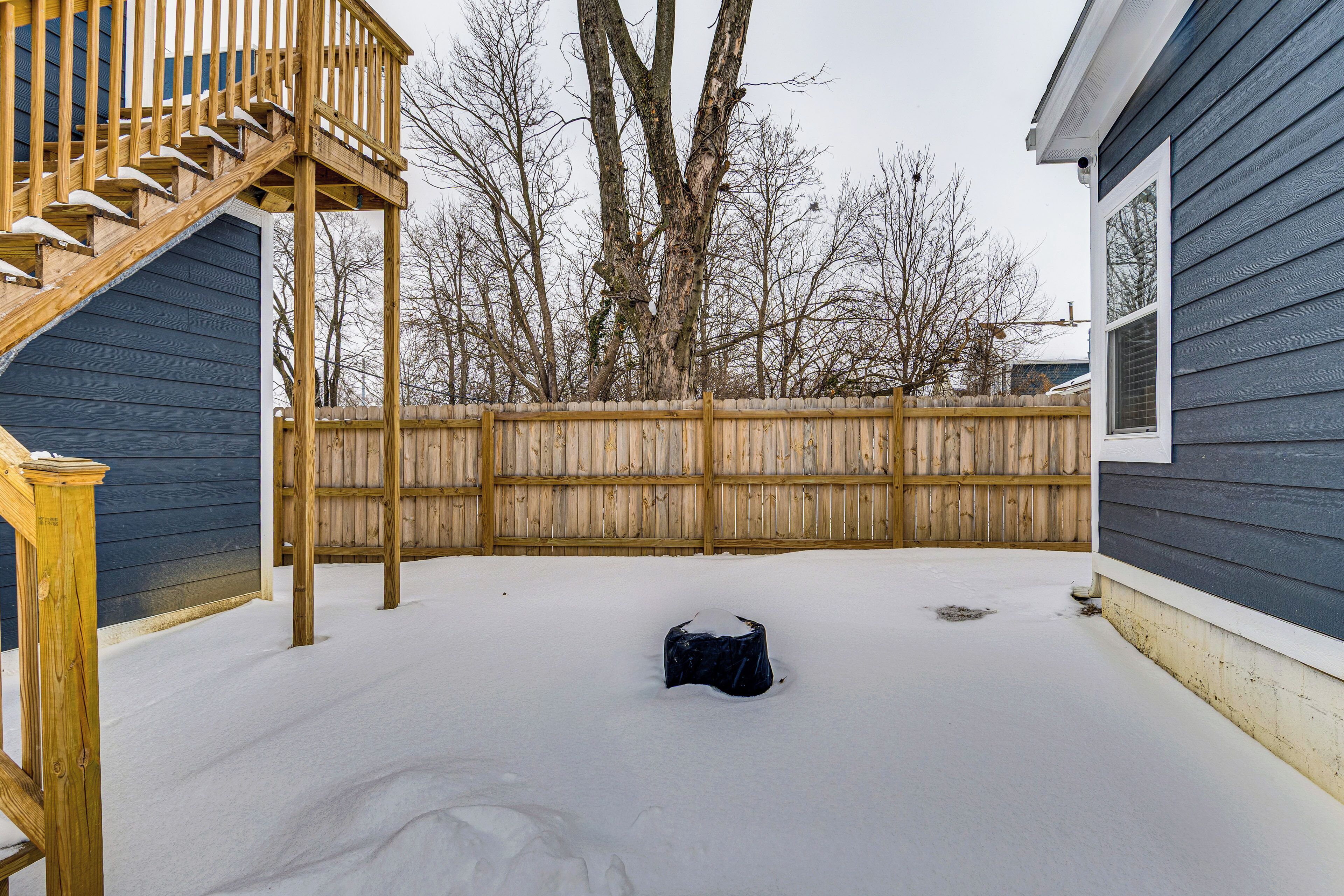 A backyard with a wooden deck, a covered object, and a wooden fence.