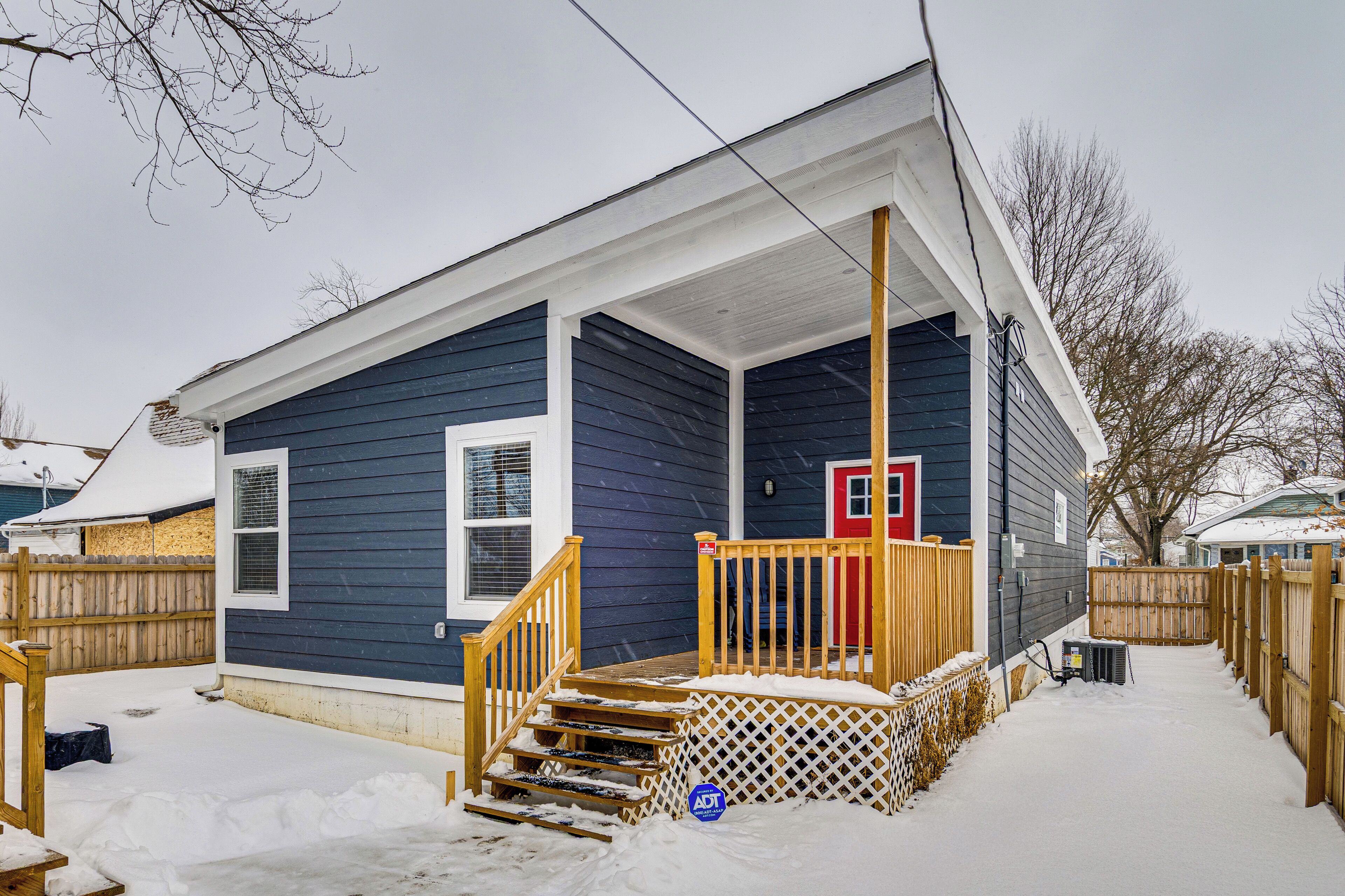 A two-story house with a covered porch, wooden steps, and a red door.