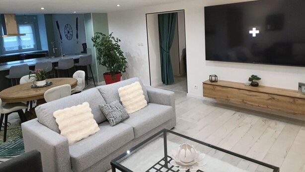 A modern living room with a grey sofa, a coffee table, and a TV on the wall.