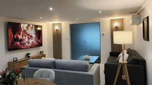 A modern living room with a sofa, a dining table, and a TV displaying a fireplace.