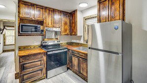 Une cuisine compacte dotée de meubles en bois, d  ’appareils électroménagers en acier inoxydable, notamment un four à micro-ondes, une cuisinière et un réfrigérateur, ainsi que d’une fenêtre avec des stores.