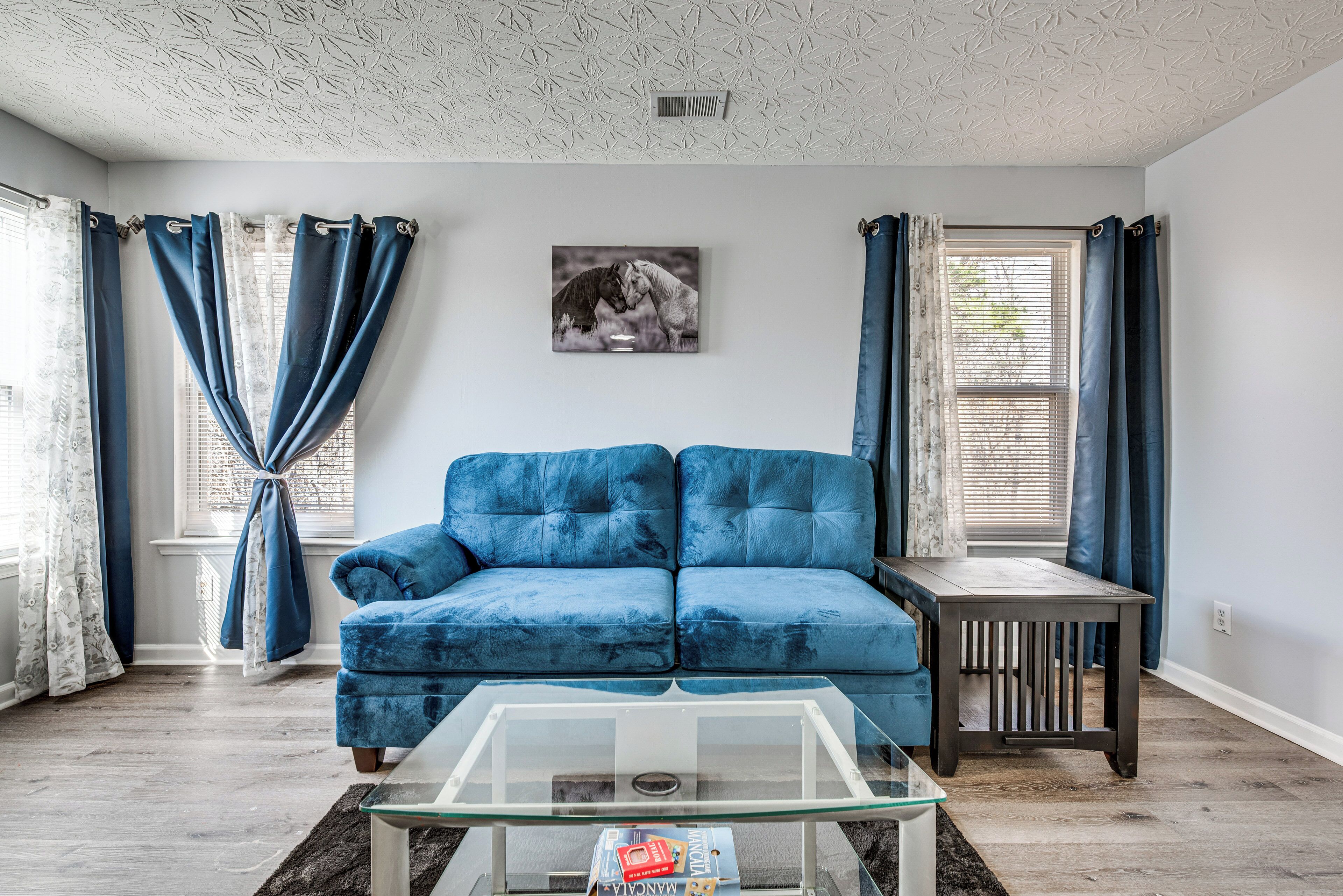 A living room with a blue sofa, a glass coffee table, and a painting on the wall.