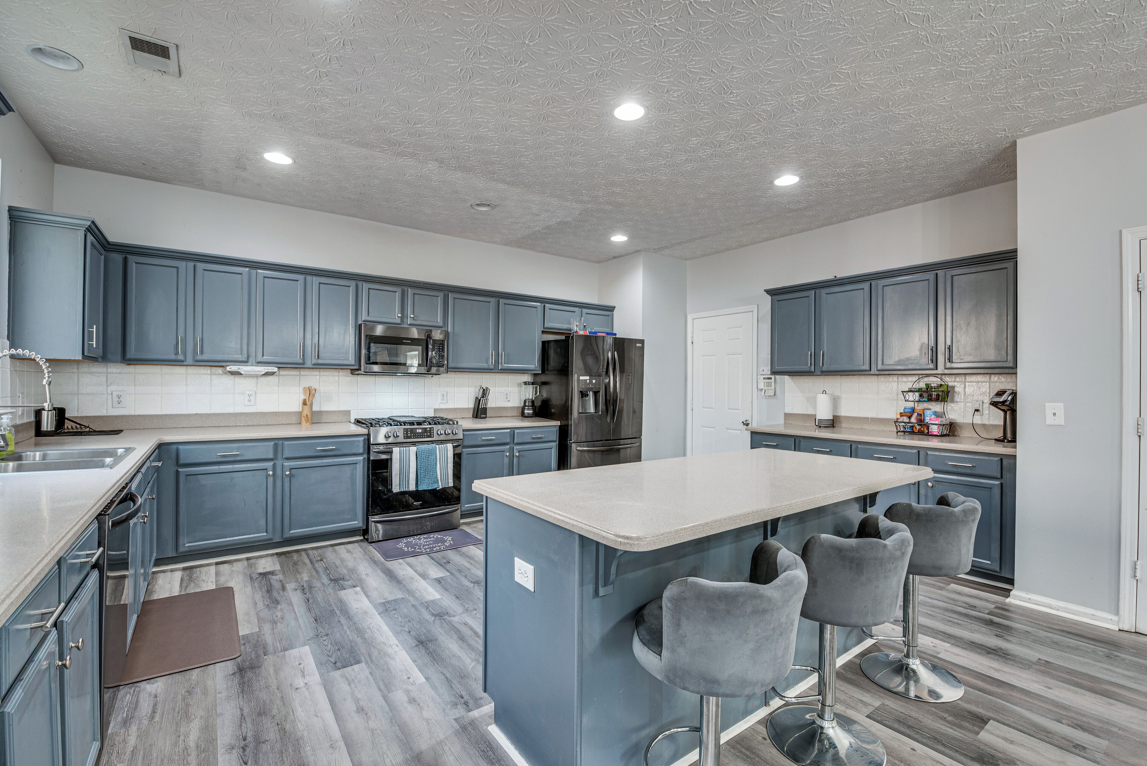 A modern kitchen with blue cabinets, stainless steel appliances, and a central island with bar stools.