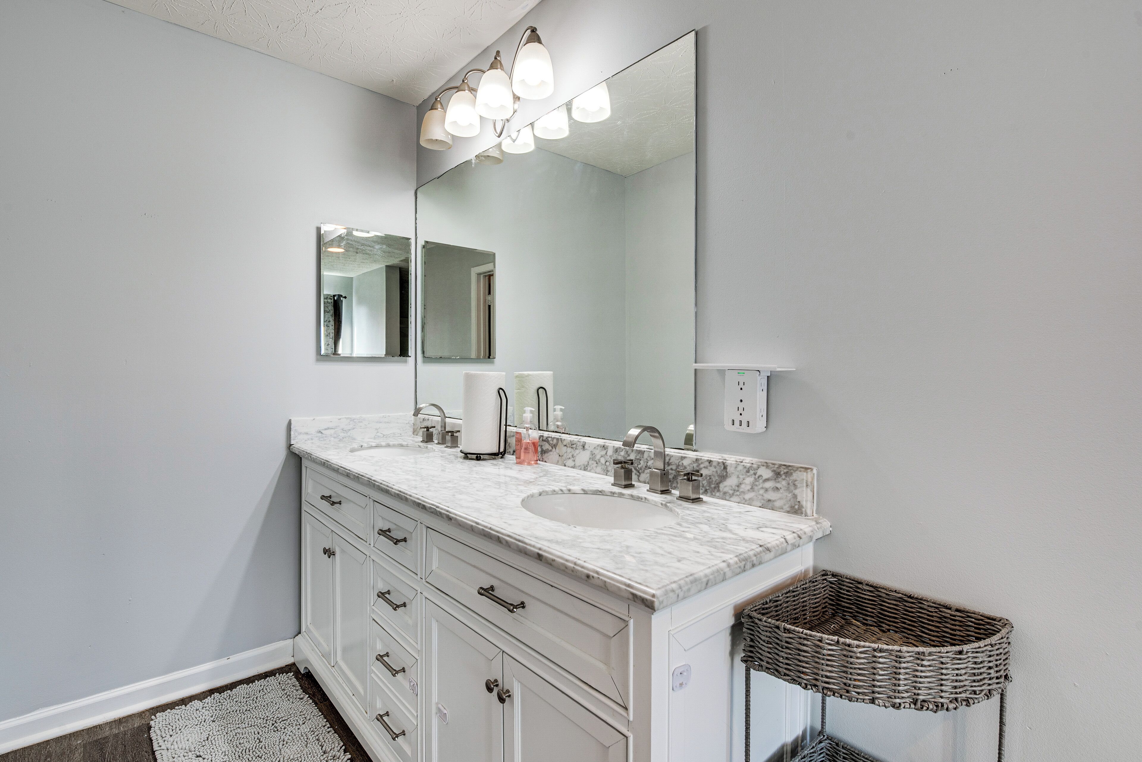 A bathroom with a large mirror, two sinks, a white vanity, and a wicker basket.