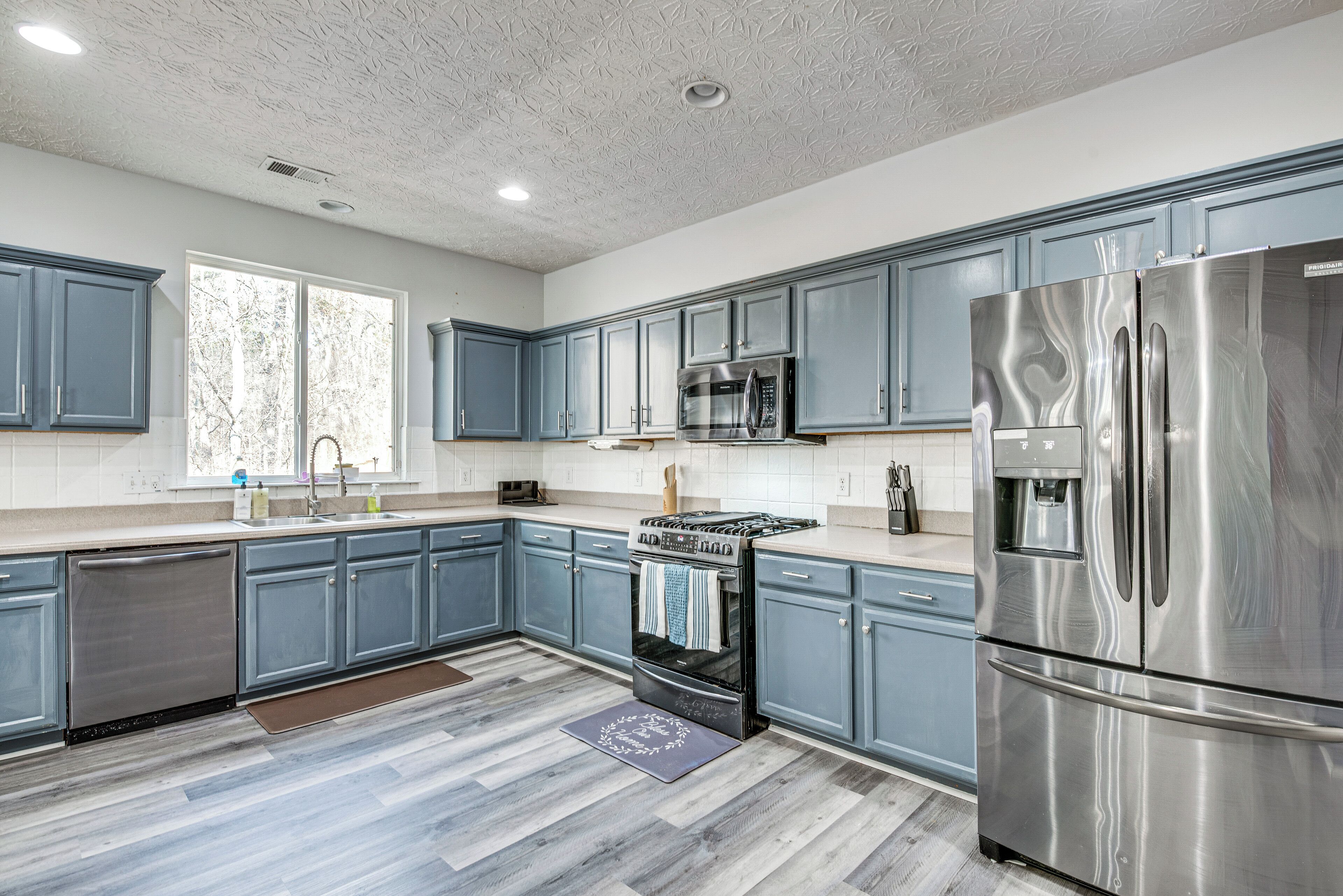 A modern kitchen with blue cabinets, stainless steel appliances, and a wooden floor.