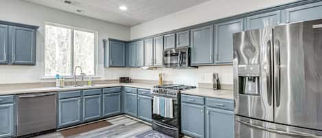 A modern kitchen with blue cabinets, stainless steel appliances, and a wooden floor.
