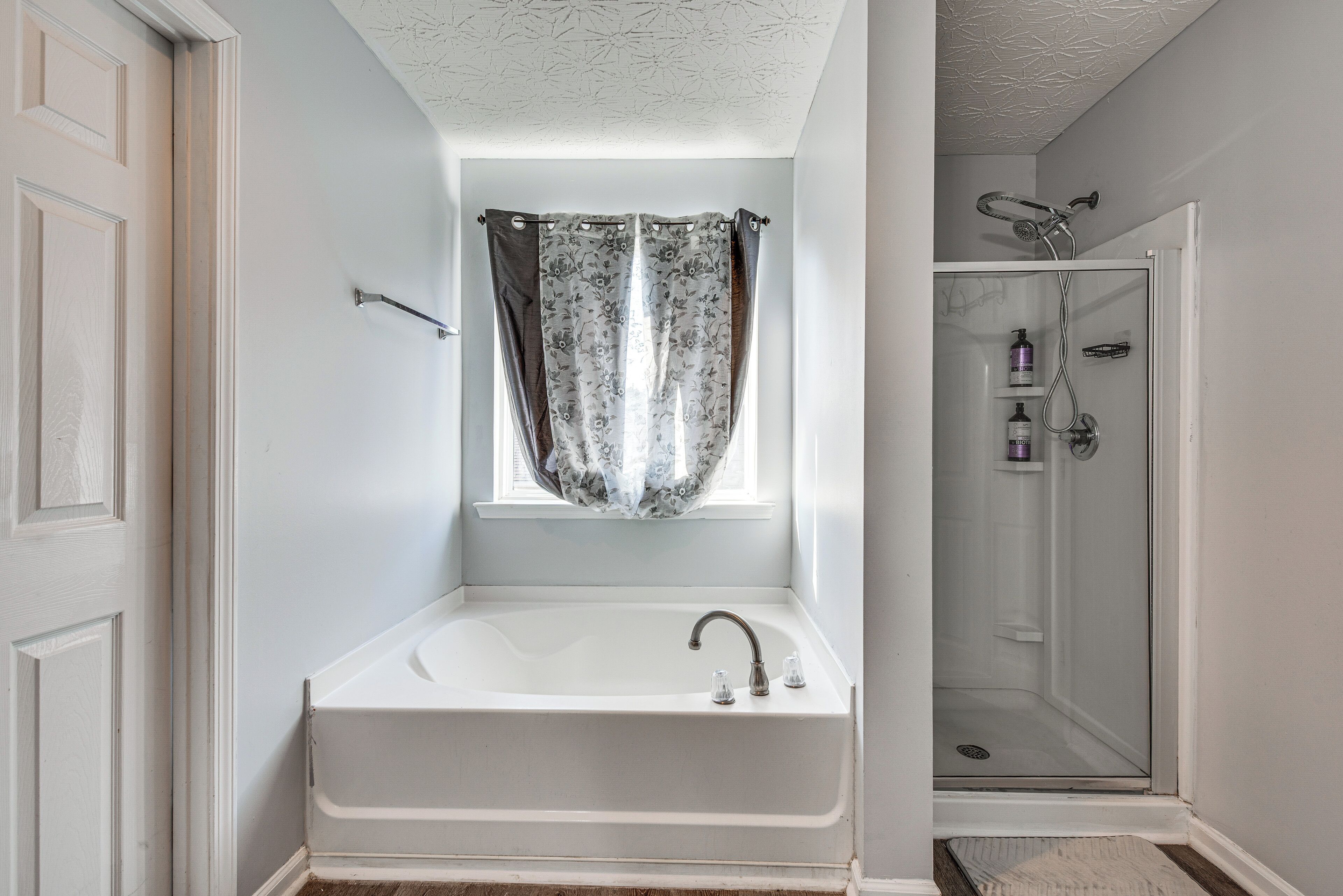 A bathroom with a bathtub, a shower, and a window with a curtain.