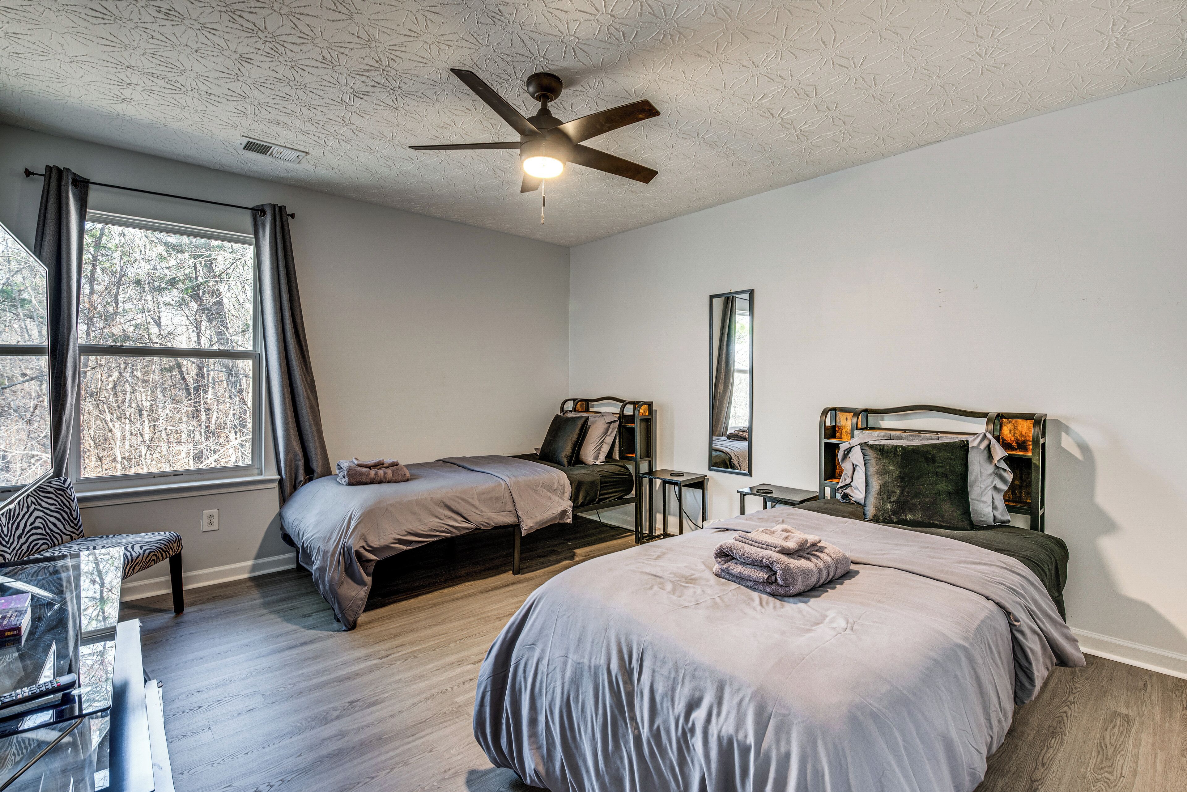 A bedroom with two beds, a ceiling fan, a window with curtains, a mirror, and a small table.