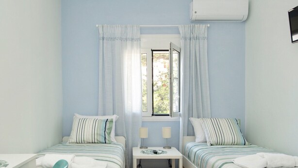 A bedroom with two single beds, a desk, a chair, a nightstand, and an air conditioning unit. - Naoussa Apricot Garden, 5' to Center, 5' to Beach (Naousa)