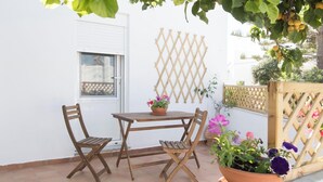 A patio with a wooden table and two chairs, a potted plant with flowers, and a wooden lattice wall. - Naoussa Apricot Garden, 5' to Center, 5' to Beach (Naousa)