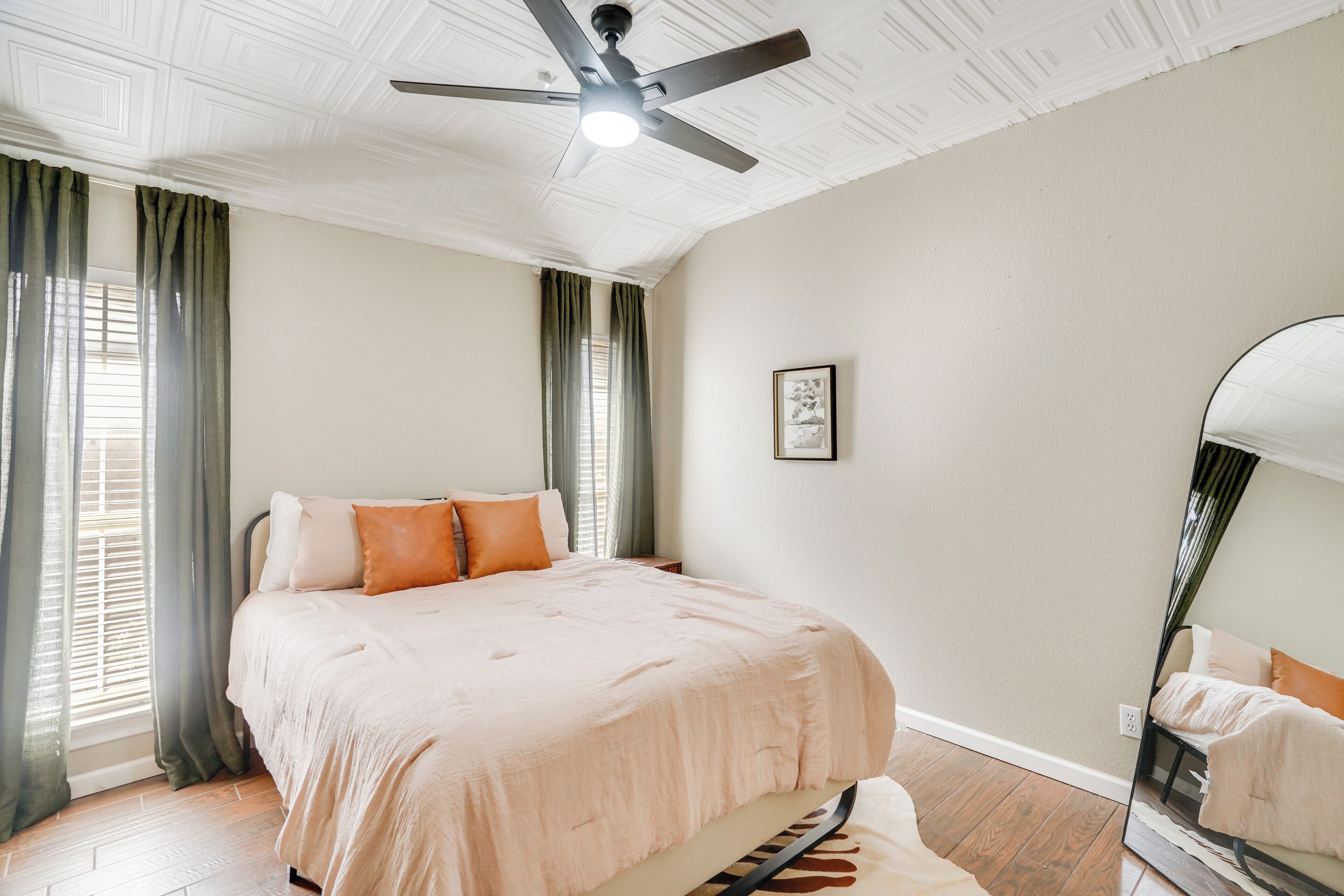 A bedroom with a bed, a ceiling fan, a large mirror, and a framed picture on the wall.