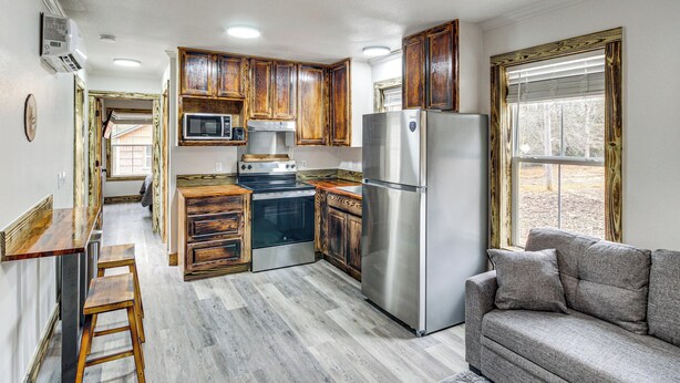 A kitchen with wooden cabinets, stainless steel appliances, a bar counter, and a gray sofa. - Gulfport Cottage w/ Fire Pit: Relax & Recharge! (Gulfport)