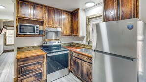 A kitchen with wooden cabinets, a stainless steel refrigerator, a microwave, a stove, and a dishwasher. - Gulfport Cottage w/ Fire Pit: Relax & Recharge! (Gulfport)