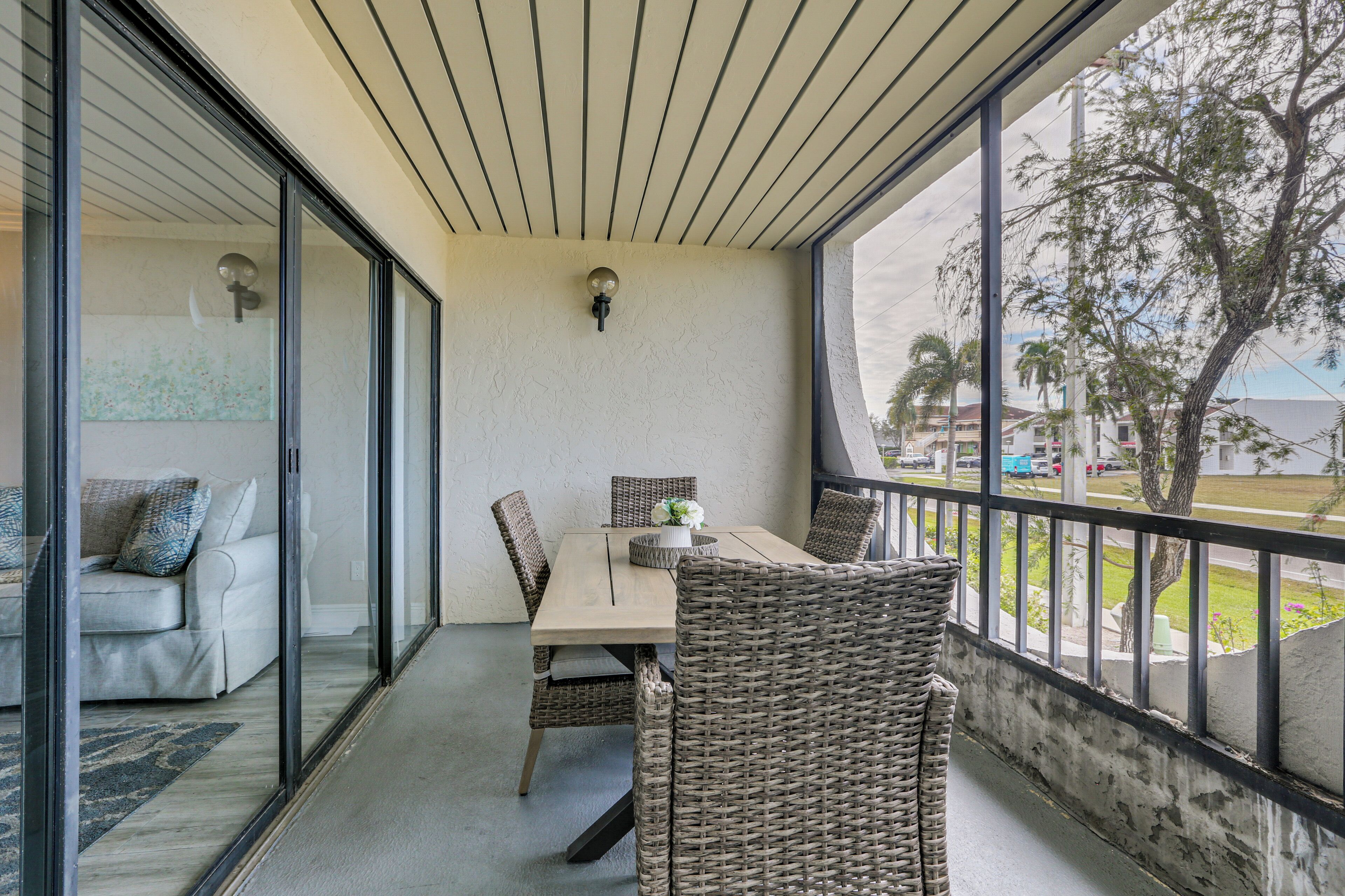 A balcony with a dining table and wicker chairs, a sofa, and a view of the street and trees.
