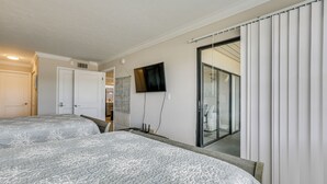 Ein Schlafzimmer mit zwei Betten, einem Fernseher, einer Schiebetür und Balkonblick.