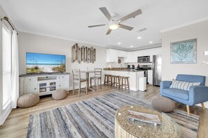 A modern kitchen with white cabinets, a dining area with a large TV, and a blue sofa. - ☀️Balcony | Walk to Beach | 30A | Gulf Place Caribbean 406☀️ (Santa Rosa Beach)