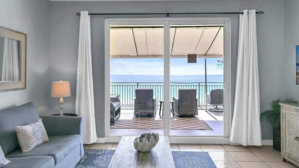 Ein Zimmer mit einer Couch, einem Tisch mit einer dekorativen Schale, einer Lampe und Blick auf einen Balkon mit Stühlen und Tisch.