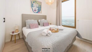 A bedroom with a large bed, a city view, a painting on the wall, and a small side table. - O’Searys - stylish apartment with stadium view (Oostende)