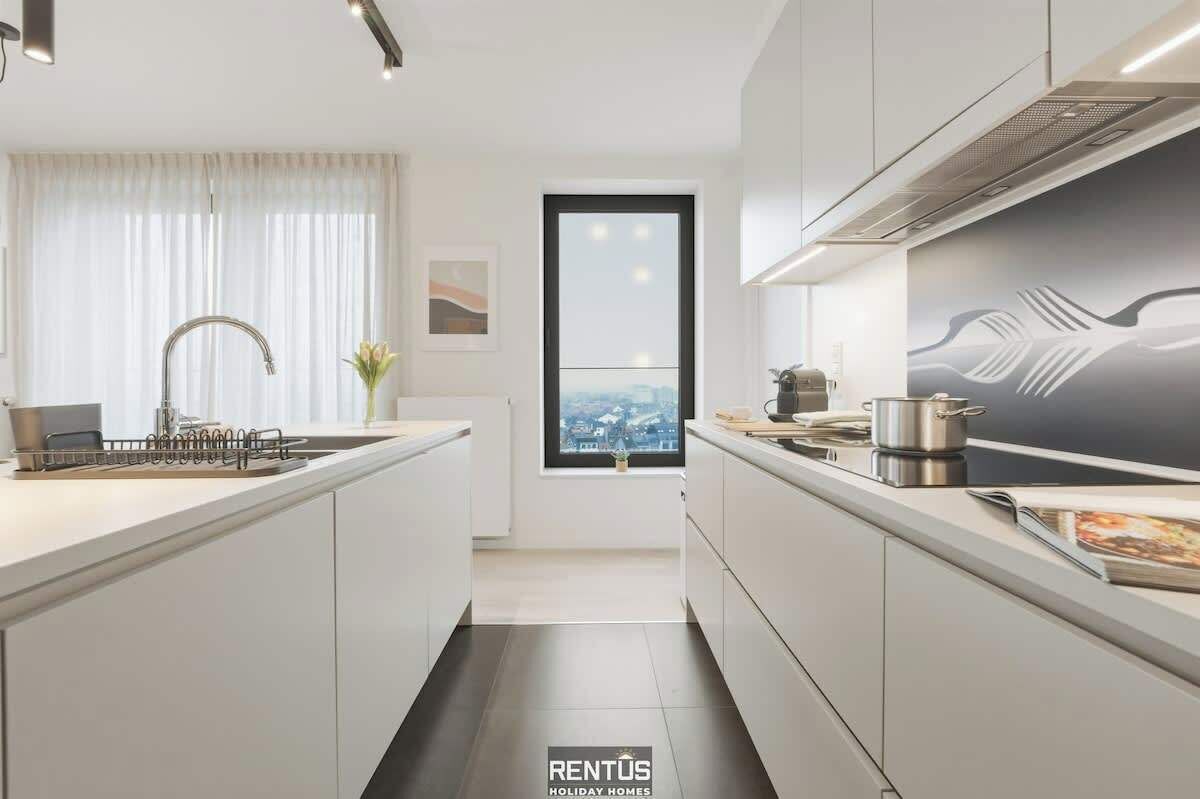 Een moderne keuken met een centraal eiland, een raam met uitzicht over de stad, en een groot schilderij aan de muur.