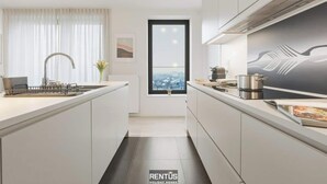 A modern kitchen with a central island, a window with a city view, and a large painting on the wall. - O’Searys - stylish apartment with stadium view (Oostende)
