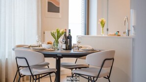 A dining area with a round table set for two, a vase with flowers, and a bottle of wine. - O’Searys - stylish apartment with stadium view (Oostende)