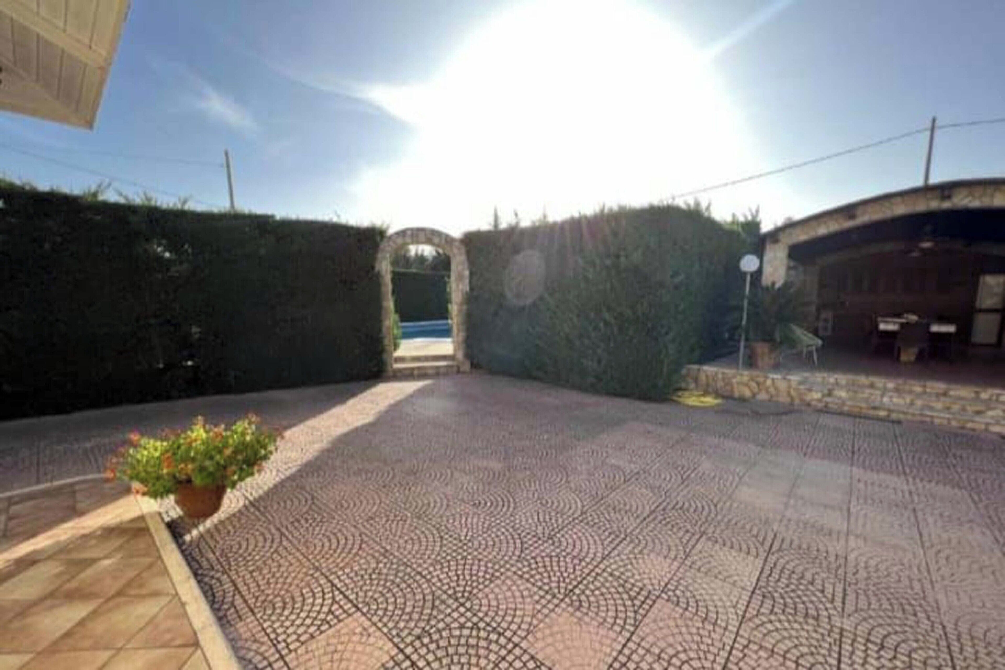 Une cour dallée, dotée d’un sol carrelé à motifs, entourée de haies et d’un mur en briques.