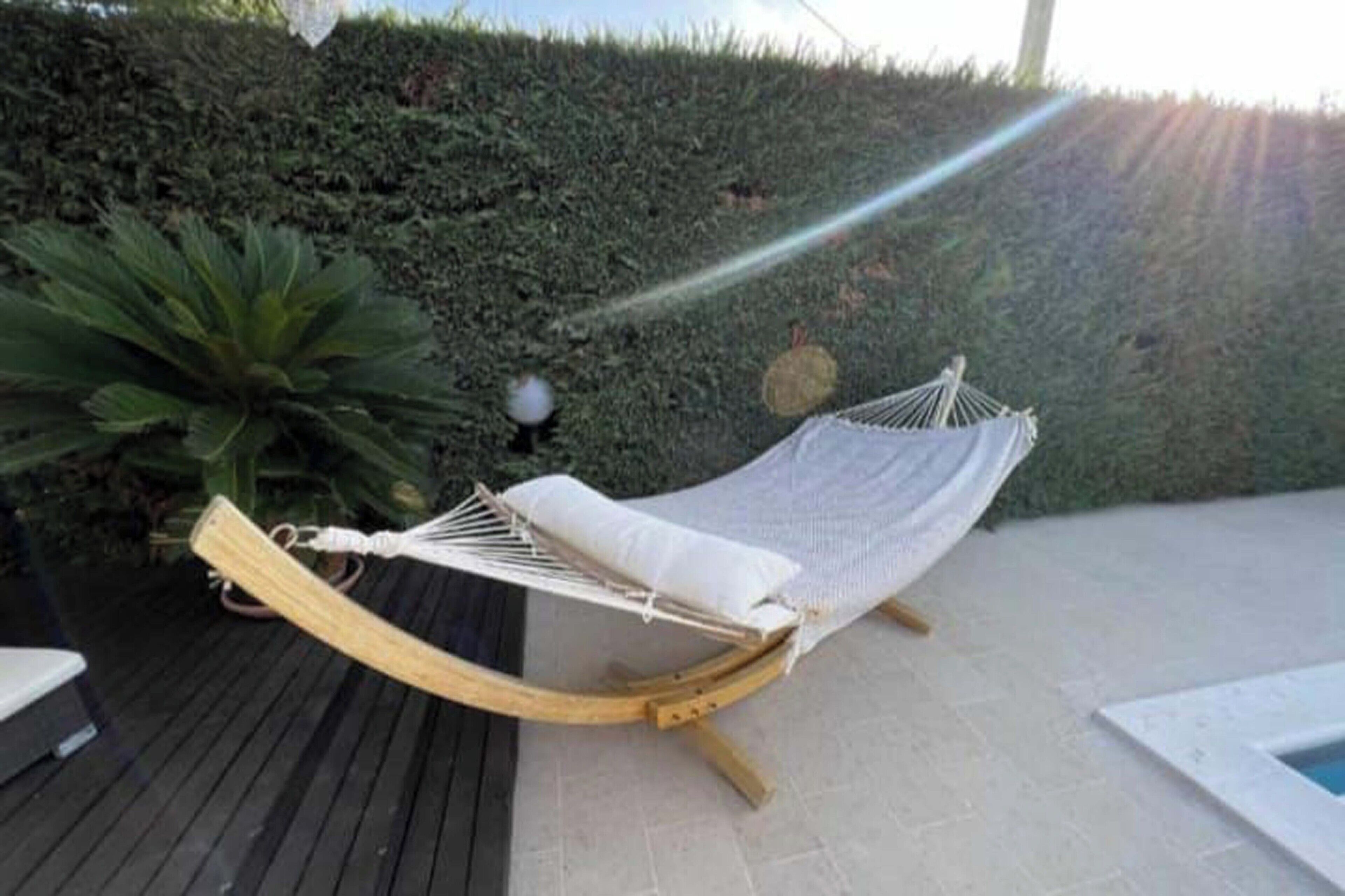 Una silla hamaca con cojín blanco, estructura de madera y un tapete blanco sobre una terraza de madera.