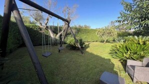 A wooden swing set in a well-maintained grassy yard with a hedge and a chair. - Villa sole cozy villa located in the countryside cica 3 km from town (SAN VITO DEI NORMANNI)