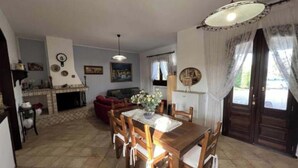A dining area with a wooden table and chairs, a fireplace, and a sofa in the background. - Villa sole cozy villa located in the countryside cica 3 km from town (SAN VITO DEI NORMANNI)
