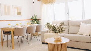Un soggiorno luminoso con divano, tavolino rotondo e zona pranzo con sedie e tavolo apparecchiato per la colazione.