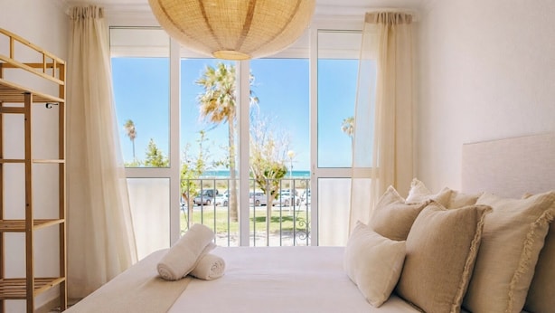 Camera d'hotel con un letto grande, una scala in legno e vista sulla spiaggia e palme.