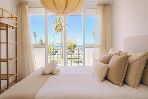 A hotel room with a large bed, a wooden ladder, and a view of the beach and palm trees. - Villa Rosa primera linea (Conil de la frontera)