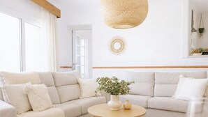 Un soggiorno moderno con un divano modulare beige, un tavolino da caffè rotondo in legno e una lampada a sospensione intrecciata.