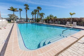 A rectangular swimming pool with clear blue water, surrounded by a brick deck and palm trees. - Waterfront Townhome with Stunning Intracoastal Views (Treasure Island)