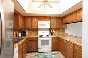 A compact kitchen with wooden cabinets, a microwave, an oven, and a ceiling fan. - Waterfront Townhome with Stunning Intracoastal Views (Treasure Island)