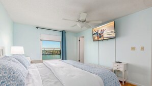 Ein Schlafzimmer mit einem Bett, einem Nachttisch, einem Fernseher, einem Fenster mit Blick und einem Deckenventilator.