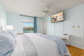 A bedroom with a bed, a nightstand, a TV, a window with a view, and a ceiling fan. - Waterfront Townhome with Stunning Intracoastal Views (Treasure Island)