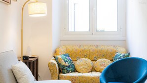 Ein Zimmer mit einer blumigen Couch, einem blauen Sessel, einer Lampe und einem kleinen Tisch mit einer Flasche.