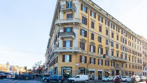 Ein mehrstöckiges Gebäude mit Balkonen, eine Klinik im Erdgeschoss und parkende Autos an der Straße.