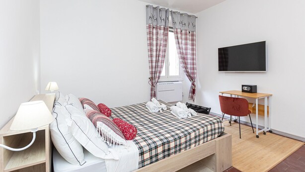Ein Schlafzimmer mit Bett, Nachttisch, Lampe, Fernseher und Schreibtisch mit Stuhl.