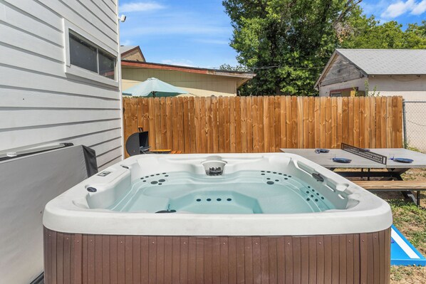 A hot tub in a backyard with a wooden fence, a picnic table, and a covered umbrella.