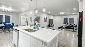 A modern kitchen with a central island, pendant lighting, and a dining area with blue chairs. - Gorgeous 6BR Sleeps 16 with Hot Tub, BBQ, Games, Big Screen TV.  Near Downtown (San Antonio)