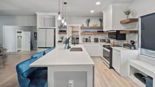 A modern kitchen with white cabinetry, a central island, and pendant lighting. - Gorgeous 6BR Sleeps 16 with Hot Tub, BBQ, Games, Big Screen TV.  Near Downtown (San Antonio)
