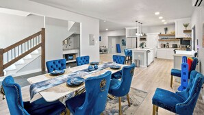 A modern dining area with a wooden staircase, blue upholstered chairs, and a central island. - Gorgeous 6BR Sleeps 16 with Hot Tub, BBQ, Games, Big Screen TV.  Near Downtown (San Antonio)